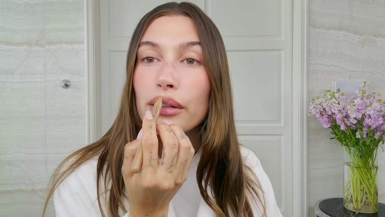 Hailey Bieber cleaning up the lip outline with a fingertip